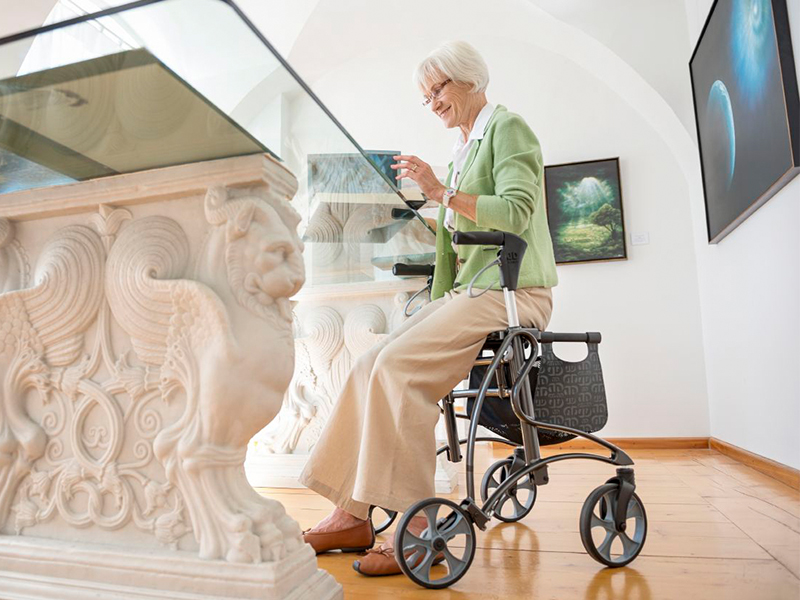 Frau sitzt auf Leichtgewichtrollator Dolomite Jazz von Invacare und liest eine Zeitschrift