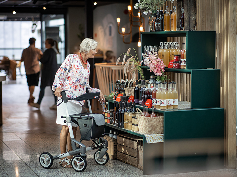 Frau steht mit Leichtgewichtrollator Troja von Topro vor einem Schaufenster