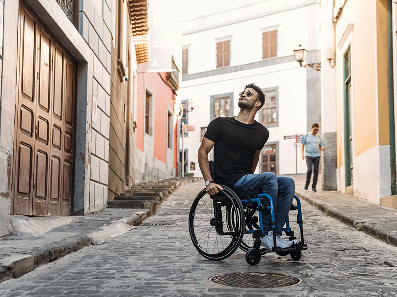 Mann sitzt auf einer gepflasterten Straße in einem Aktivrollstuhl und schaut in die Luft